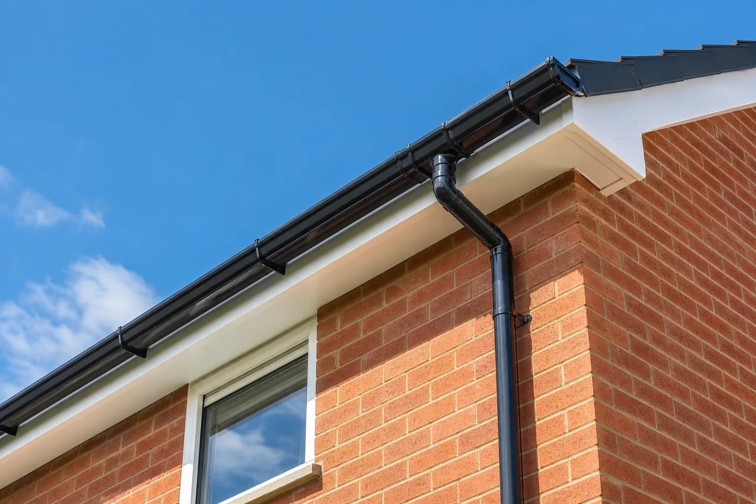 New black uPVC guttering and downpipe fitted to the eaves of a brick house